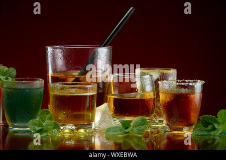 Verschiedene alkoholische Cocktails in klare Gläser mit Eis und Minze auf rotem Hintergrund Stockfoto