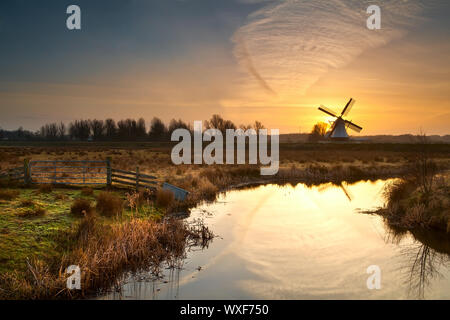 Holländische Windmühle bei Sonnenaufgang spiegelt sich im Fluss Stockfoto