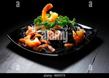 Schwarze Spaghetti mit Meeresfrüchten am schwarzen Tisch Stockfoto