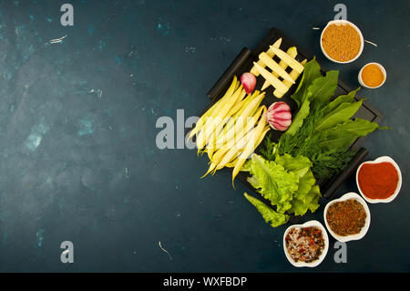 Das GEMÜSE IN DER BOX AUF DEM STEIN einen dunklen Hintergrund. Die jungen grünen Zwiebeln Knoblauch ZUCCHINI HELLE GEWÜRZE LAG IN EINEM HOLZ- fach Stockfoto