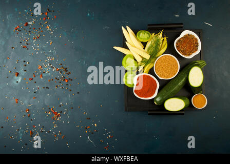 Das GEMÜSE IN DER BOX AUF DEM STEIN einen dunklen Hintergrund. Die jungen grünen Zwiebeln Knoblauch ZUCCHINI HELLE GEWÜRZE LAG IN EINEM HOLZ- fach Stockfoto