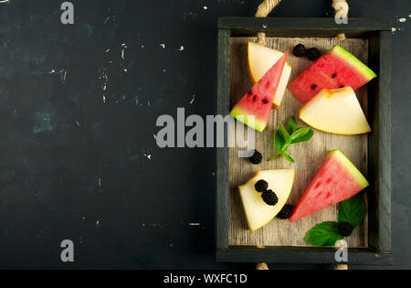 Wassermelone Melone BROMBEEREN MINT IN DER BOX IN DEN HINTERGRUND. Drei Stücke REIFE WASSERMELONE SAFTIGE MELONE MIT REIF BLACKBERR Stockfoto