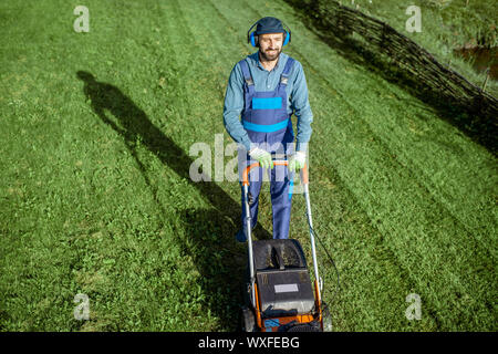 Professionelle Gärtner in arbeitsschutzausrüstungen Schneiden von Gras mit Benzin Rasenmäher auf den Hinterhof Stockfoto
