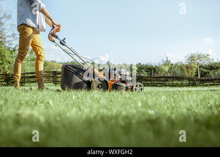 Man Schneiden von Gras mit Benzin Rasenmäher auf dem Hinterhof, 7/8-Bild ohne Gesicht Stockfoto