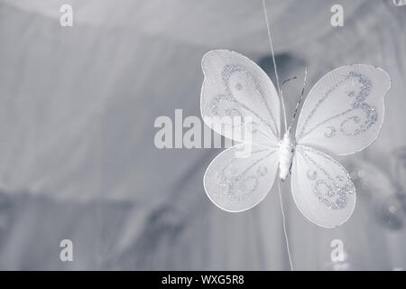 Nahaufnahme des hängenden handgemachten weißen Schmetterling mit Silber glänzt aus transparentem Material. Selektive konzentrieren. Kopieren Sie Raum auf der linken Seite. Stockfoto