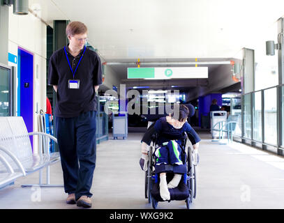 Vater gehen mit behinderten Sohn im Rollstuhl, wie er die Räder sich in das Krankenhaus Eingang Stockfoto