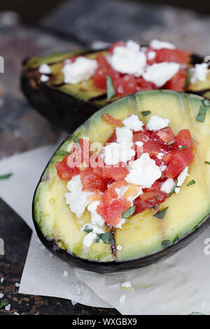 Gegrillte Avocados mit gewürfelten Tomaten und Feta Käse gefüllt und mit Olivenöl garniert und frisch gehackte Petersilie. Stockfoto