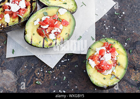 Gegrillte Avocados mit gewürfelten Tomaten und Feta Käse gefüllt und mit Olivenöl garniert und frisch gehackte Petersilie. Stockfoto