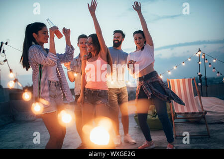 Gerne Freunde mit Getränken Schiebeschalter auf der Dachterrasse bei Nacht Stockfoto