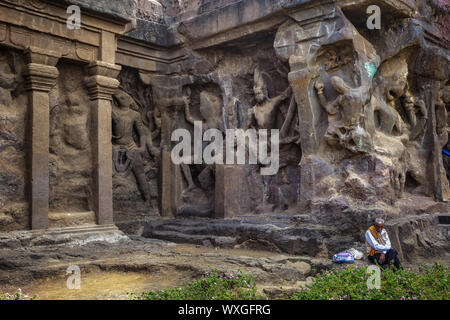 Ellora, Maharashtra, Indien - Januar 15, 2018: Ellora Höhlen. Ein Mann sitzt in der Nähe der Wände eines antiken Tempels Stockfoto