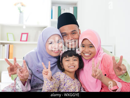 Glückliche asiatischen Familie zu Hause. Muslimische Familie V Siegeszeichen Hand zeigen und Spaß zu haben. Südostasiatische Eltern und Kinder Lächeln. Stockfoto