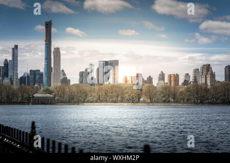 Ein Schuss von Central Park während einer schönen sonnigen Tag, mit Gebäude in das Wasser eines Sees widerspiegelt. New York City, United States