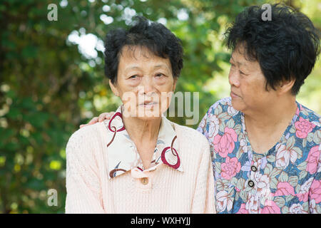 Reportageaufnahme eine asiatische Reife Frau trösten weinende alte Mutter im Outdoor-natürlichen grünen Park. Stockfoto