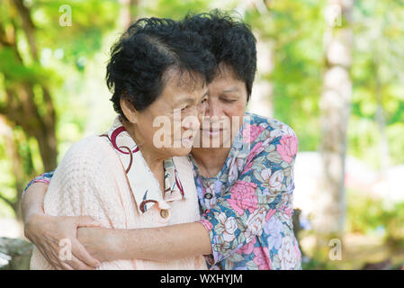 Reportageaufnahme eine asiatische Reife Frau umarmt und tröstet weinende alte Mutter bei Outdoor-Naturpark. Stockfoto