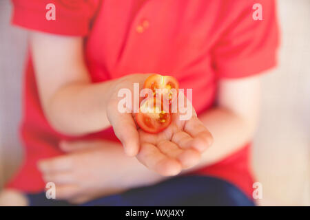 Junge Holding eine halbe Kirsche Tomate Stockfoto