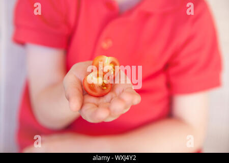 Junge Holding eine halbe Kirsche Tomate Stockfoto