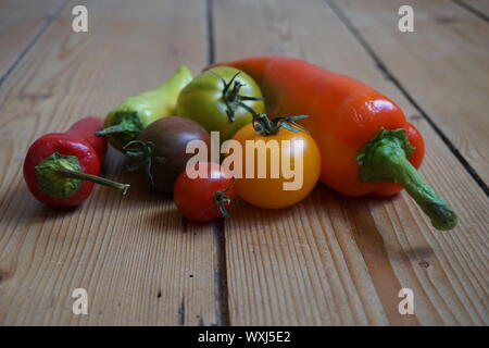 Eingestellt von bunten langen Paprika und heirloom Tomaten auf einem rustikalen Holztisch Stockfoto
