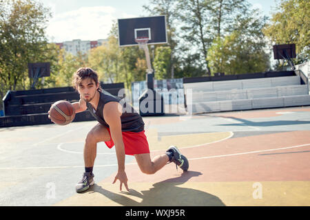 Bild des Athleten im blauen T-Shirt Basketball spielen auf dem Spielplatz im Sommer am Nachmittag Stockfoto