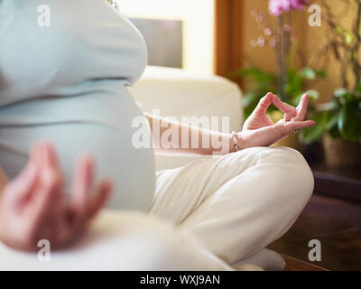 7/8-Ansicht der italienischen 6 Monate schwanger Frau mit gekreuzten Beinen Yoga Übung zu Hause sitzen. Horizontale Form, engen Fokus Stockfoto