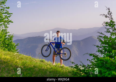 Müde Radfahrer wischte seine Schweiß aus seinem Gesicht, während sein Fahrrad bergauf schieben ein Feldweg in einem Berg. Stockfoto