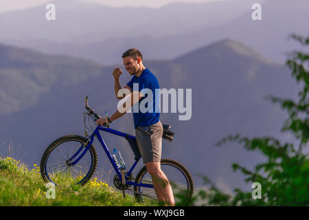 Müde Radfahrer wischte seine Schweiß aus seinem Gesicht, während sein Fahrrad bergauf schieben ein Feldweg in einem Berg. Stockfoto