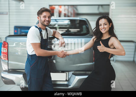 Junge schöne Mechaniker und schöne Frau client Händeschütteln in der Dankbarkeit für einen tollen Service sie zeigt wie unterzeichnen. Stockfoto