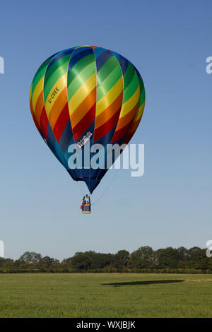 Eine glänzende Regen - verbeugte sich farbige Heißluftballon, über Felder und Bäume auf einer klaren Sommer Morgen fliegen. Perfekt Stockfoto