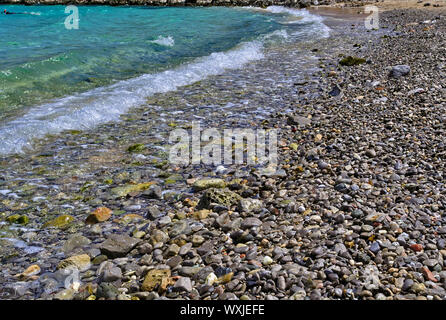 Stone beach low angle view, pebbles and turquoise sea water, snorkeler swimming. Agia (Saint) Dynami Chios island, Greece. Stockfoto