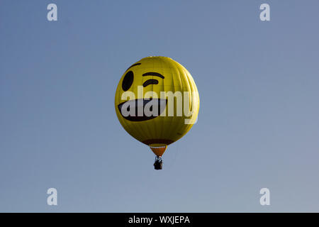 Eine gelbe glücklich, winking emoji Heißluftballon vor blauem Himmel fliegen. Smiley. 2 Stockfoto