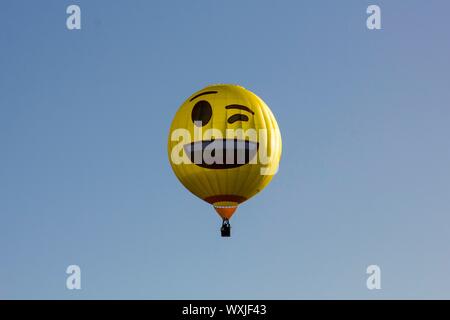 Eine gelbe glücklich, winking emoji Heißluftballon vor blauem Himmel fliegen. Smiley. 2 Stockfoto