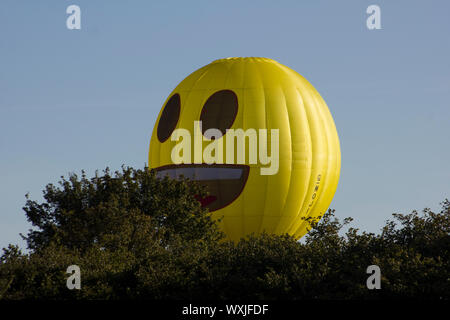 Eine gelbe glücklich emoji Heißluftballon fliegen durch die Bäume. Smilies. Lustig Stockfoto