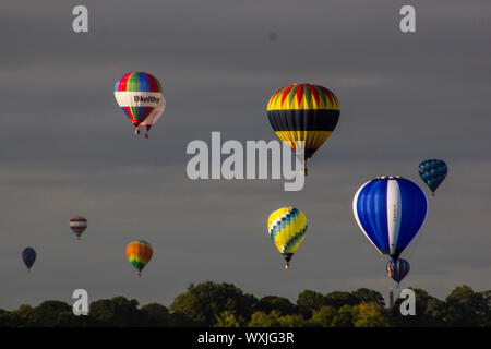 Eine Sammlung von bunten Ballons fliegen gegen etwas stürmischen Wolken, gerade über eine baumgrenze Stockfoto