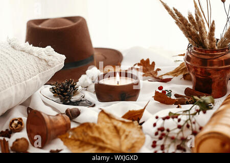 Hygge Lebensstil. Kerze, Beeren, fallen, Blätter, Kräuter, Eicheln, Nüsse und braunen Hut auf weißem Stoff. Herbstliche Stimmung. Hallo Herbst, gemütliche inspirierende Bild. Stockfoto