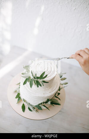 Frau Dekorieren ein Zwei mehrstufige Hochzeitstorte mit Olivenzweigen Stockfoto