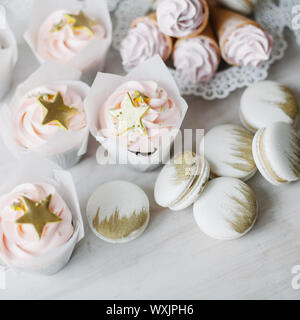 Kleine Kuchen, Waffeln mit Sahne und Makronen mit goldfarbenen Verzierungen Stockfoto