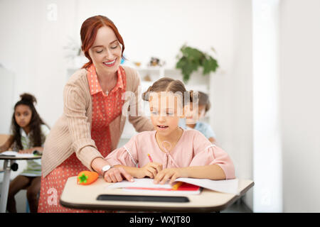 Lächelnd Lehrer helfen Mädchen mit Briefe schreiben Stockfoto