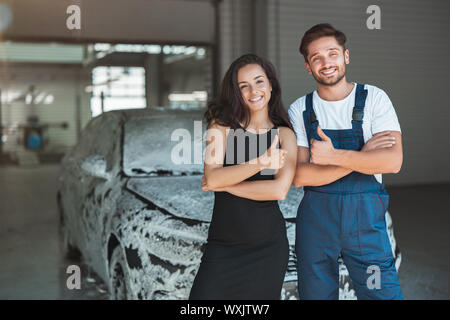 Jungen gutaussehenden Mann in Uniform und schöne Frau Client stehen in car wash Station angezeigt wie Zeichen. Stockfoto