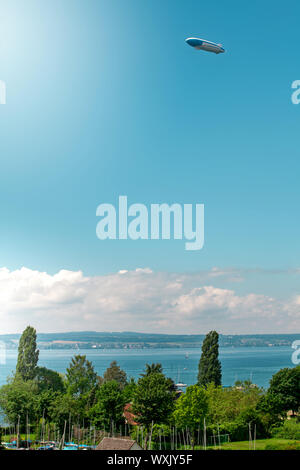 Panoramablick auf den Bodensee. Zeppelin, Apfelbäume und die Katholische Kirche St. Johann Baptist in Hagnau am Bild. Stockfoto