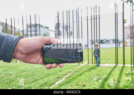 Berlin, Deutschland. 09 Sep, 2019. Eine Hand hält ein Smartphone in der Bernauer Straße. Auf der Anzeige sehen Sie, dass genau an dieser Stelle die Mauer zu diesem Zeitpunkt stand. Am 30. Jahrestag des Falls der Berliner Mauer, viele sind auf den Markt kommen. Mit der App "auAR' können Sie in die Vergangenheit bewegen und sehen, wo die Wand oder einen Turm, indem Sie die Kamera auf die entsprechende Zone stand, wie hier an der Wand Memorial. Quelle: Annette Riedl/dpa-Zentralbild/ZB/dpa/Alamy leben Nachrichten Stockfoto