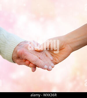 Senior Lady Hand in Hand mit jungen Frau auf rosa Lichter Hintergrund Stockfoto