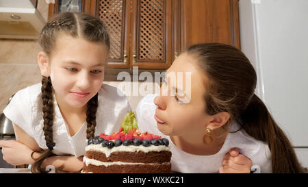 Portrat von Mutter und Tochter schnüffeln zubereitet hausgemachte Schokolade Torte mit Blaubeeren, Himbeeren und Physalis in der Küche zu Hause. Jugendlich Mädchen nimmt Berry aus dem Kuchen und essen es. Stockfoto