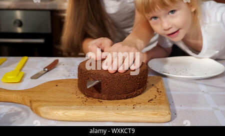 Family Portrait von Mutter und Töchter bereiten Geburtstag Kuchen zusammen, Mom ist Schneiden Biskuitteig mit Messer in der Küche. Stockfoto