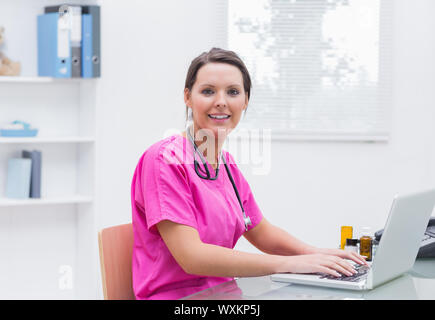 Porträt der lächelnde junge Krankenschwester mit Laptop am Schreibtisch in Klinik Stockfoto