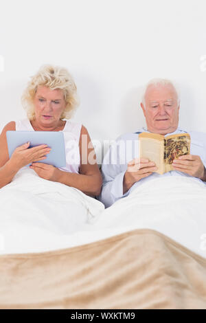 Altes Paar lesen oder mit einem digitalen Tablet auf dem Bett Stockfoto