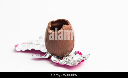 Osterei ausgepackt in rosa Folie mit Biss herausgenommen, auf weißem Hintergrund Stockfoto
