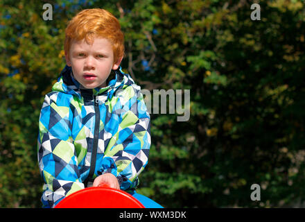 Kinder spielen am Spielplatz im Freien. Jungen spielen auf die Schule oder in den Kindergarten Hof. Kind mit Curly Ingwer Haar. Porträt. Der rothaarige Junge starrt konzentriert Stockfoto