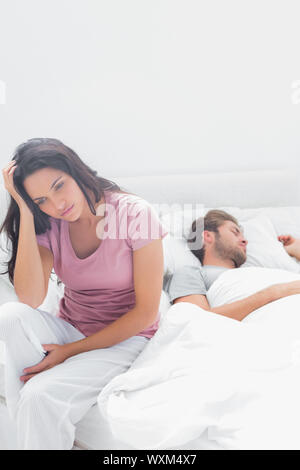 Betonte Frau denken, während sie in ihrem Bett neben ihrem Partner saß ist Stockfoto