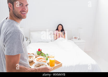 Gut aussehender Mann, seine Frau im Bett Frühstück bringen Stockfoto