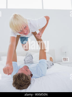 Vater spielen Flugzeug halten Sie seinen Sohn im Bett Stockfoto
