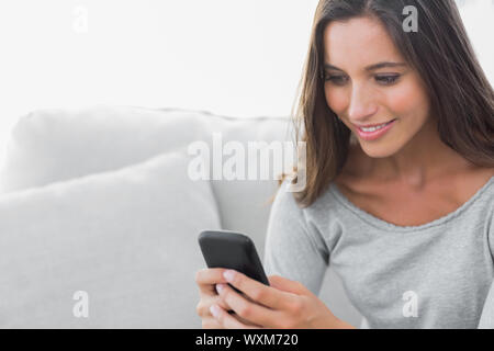 Attraktive Frau von SMS-Nachrichten, während sie auf einer Couch saß ist Stockfoto